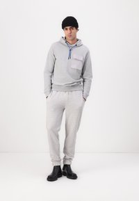 Light gray hooded sweatshirt with a front pocket, blue drawstrings, paired with light gray joggers and black ankle boots.