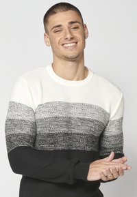 Pulover tricotat cu textură, în nuanțe de alb, gri și negru, cu un model degradé. Guler rotund, mâneci lungi și manșete ribelate pentru un detaliu suplimentar.