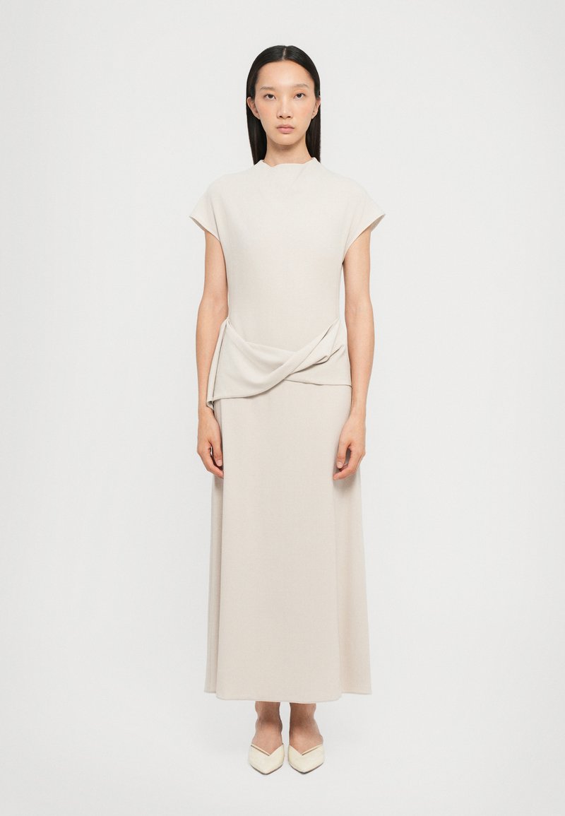 Beige dress with short cap sleeves and a draped front detail, featuring a smooth texture and fitted silhouette, paired with pointed white shoes.