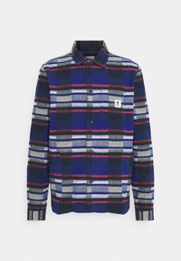 Chemise à manches longues boutonnée avec un motif à carreaux horizontaux et verticaux bleu, noir, gris, blanc et rouge, avec une poche poitrine avant et une étiquette.