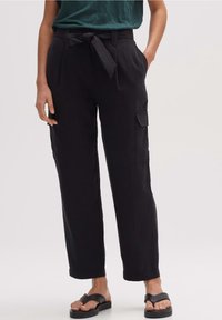 Pantalon cargo noir taille haute avec ceinture nouée, poches latérales et coupe ample. Confectionné dans un tissu doux et texturé pour plus de confort.