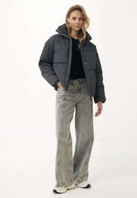 Puffjacka i mörkgrått med vita prickar, med dragkedja fram och hög krage, ihop med vida, blekta grå jeans och vita sneakers.