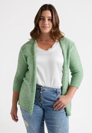 Light green cardigan with 3/4 sleeves, textured knit, and subtle sparkle details. Worn over a white top and paired with blue jeans.