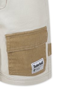 Shorts beige realizzati in un tessuto resistente, dotati di una grande tasca cargo marrone con un'etichetta bianca del logo Timberland e dettagli di cucitura rinforzata.