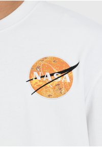 Biały sweter z pomarańczową naszywką z logo NASA, z teksturowanym wzorem planety i czarnym „swooshem” na literach.