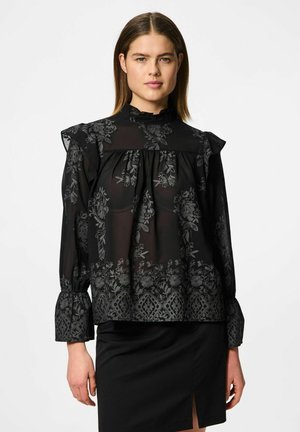 Svart genomskinlig blus med blommönster, volangärmar, långa ärmar och hög halsringning. Kombinerad med en svart figurnära kjol.
