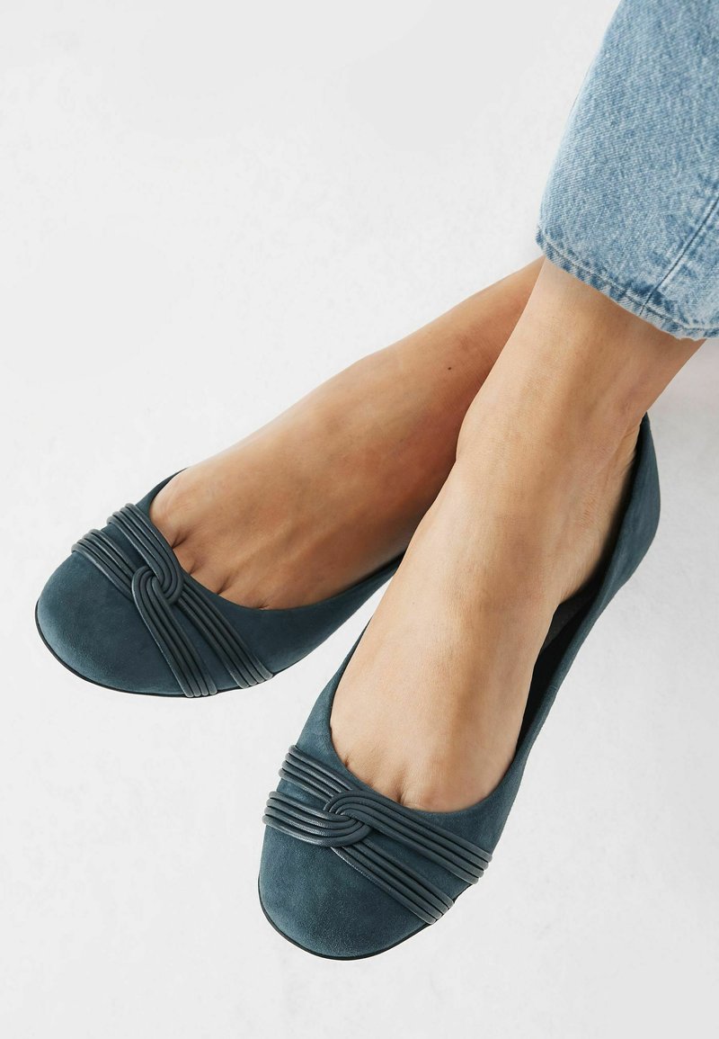 Ballerine in suede verde acqua con un design annodato sulla punta. Forma arrotondata e superficie liscia, con profilo basso e suola flessibile.