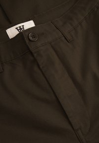 Dark brown cotton pants with a smooth texture, featuring a button closure and a white label with black text on the waistband.