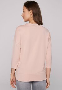 Felpa rosa chiaro, vestibilità ampia, collo rotondo, maniche a tre quarti, con orlo dritto e spacco laterale. Tessuto morbido, dettagli minimi.