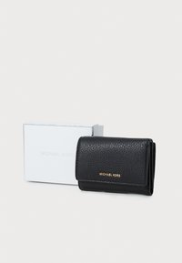 Juodas odinis piniginių su tekstūruotu paviršiumi, auksiniu logotipu, sulankstytas dizainas, padėtas šalia balto dėžutės su užrašu "MICHAEL KORS."