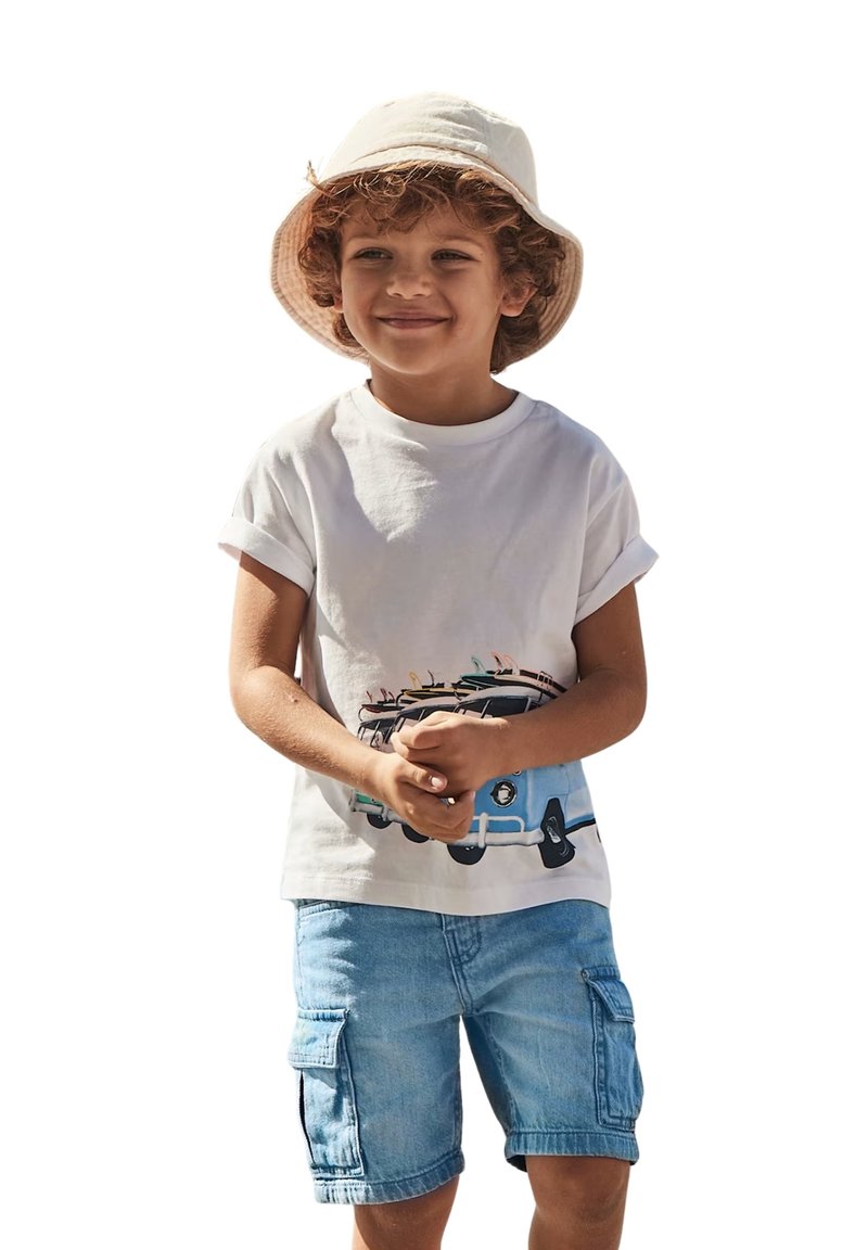 T-shirt bianco in cotone con una grafica colorata di un furgone vintage; abbinato a pantaloni cargo blu chiaro. Ragazzo con un cappello a secchiello beige.