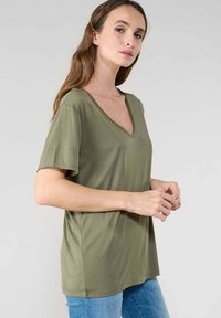 Camiseta de manga corta en verde oliva con cuello en V, hecha de una tela suave; corte relajado con una textura suave y diseño simple.
