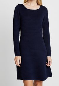 Robe bleu marine à manches longues, design côtelé texturé, encolure dégagée et surpiqûres blanches aux poignets et à l'encolure.