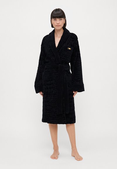 Μαύρη ρόμπα μπάνιου με υφασμάτινο ανάγλυφο σχέδιο, φαρδιά μανίκια, ζώνη και χρυσό έμβλημα στο στήθος. Απαλή, πολυτελής ύφανση.