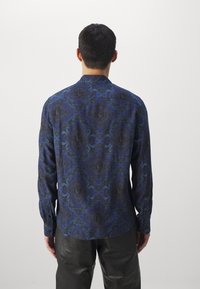 Koszula z długim rękawem wykonana z niebiesko-czarnej tkaniny w wzory, z klasycznym kołnierzykiem i zapinana na guziki z przodu, w dopasowanym kroju i o miękkiej fakturze.