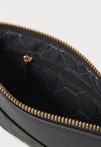 Črn usnjen denarnica z zlatim zadrgo in notranjim žepom. Notranjost obložena s črno tkanino z ponavljajočim se vzorcem "ALDO".