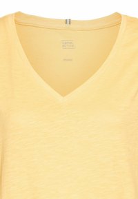 Żółta koszulka V-neck wykonana z organicznych materiałów. Miękka w dotyku, z delikatnym melanżowym wzorem i metką z logo marki "camel active."