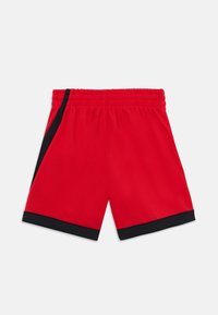 Shorts de sport rouges avec une taille élastique, présentant des accents noirs sur les côtés et un tissu lisse et léger.
