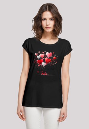 Schwarzes T-Shirt mit kurzen Ärmeln, das ein lebhaftes Herzbaum-Design in Rot und Weiß zeigt, zusammen mit dem Text "be mine". Lässige Passform.