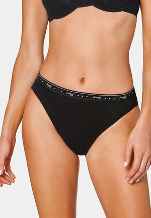 Donna che indossa slip bikini nero con fascia elastica marchiata e reggiseno nero abbinato su sfondo semplice.