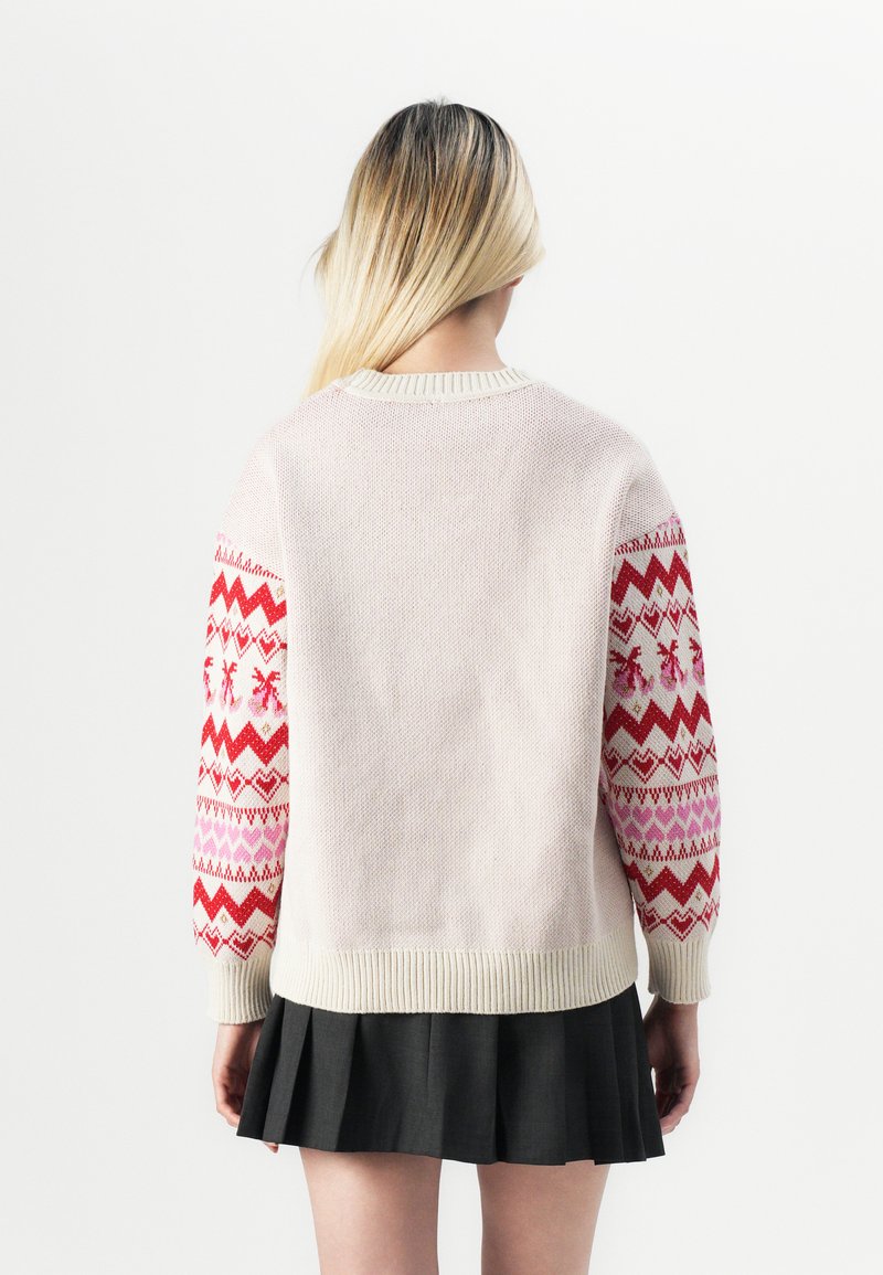 Suéter de punto en rosa pálido con mangas de un patrón vibrante en rojo y rosa. Presenta puños y dobladillo acanalados. Textura suave, corte relajado.