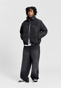 Sort puffjakke med høj krave, frontlynlås og boxy silhuet; stylet med løse sorte denimbukser og sorte sneakers.