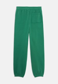 Pantalons de survêtement verts avec une taille élastique, des poignets fuselés et une poche arrière pour un confort supplémentaire. Tissu texturé visible.