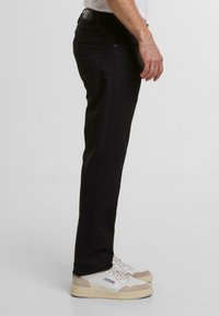 Czarne dżinsy o slim fit, z klasycznym pięciopocketowym designem i gładką fakturą. Noszone z białymi i beżowymi sneakersami.