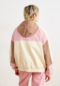 Multifarvet fløjljakke med hætte, prydet med paneler i creme, pink og brun; ribbet tekstur samt elastisk kant og manchetter.