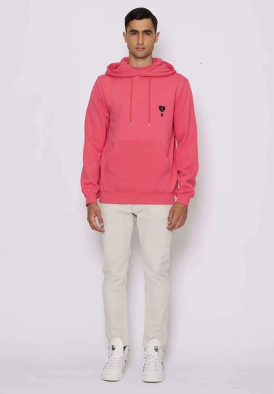 Felpa rosa con tasca a marsupio, cordini regolabili e una piccola grafica sul petto. Abbinata a pantaloni chiari e sneaker bianche.