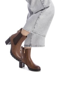 Stivali in pelle marrone alla caviglia con pannello laterale in maglia testurizzata, zip posteriore e tacco a blocco. La suola presenta un motivo di grip per una maggiore aderenza.