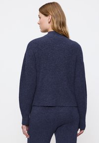 Maglione lavorato a maglia blu navy con finitura texturizzata. Presenta un colletto alto, spalle scese e un orlo dritto, abbinato a pantaloni coordinati.