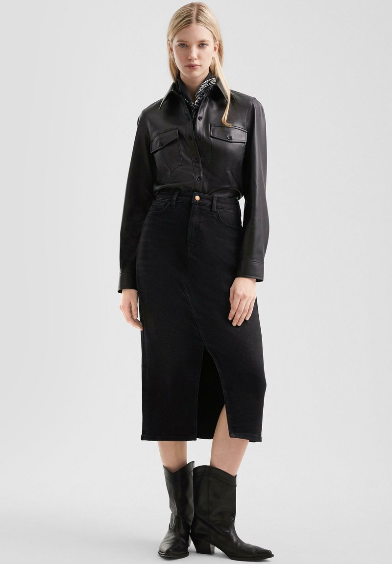 Zwarte leren knoop-overhemd met twee borstzakken, gecombineerd met een hooggewaardeerde zwarte denim midi-rok met een voorlopende splijt en cowboylaarzen.