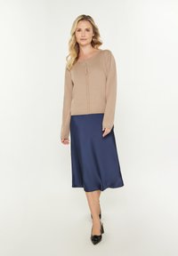 Cardigan beige in maglia con maniche lunghe e chiusura a bottoni, abbinato a una gonna midi in satin blu navy e tacchi a punta neri.
