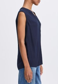 Un haut sans manches bleu marine avec une fermeture à boutons, une texture douce et un motif à côtes subtil, associé à un jean bleu clair.