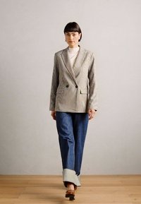 Checkered blazer in light tones, double-breasted with two buttons, paired with blue denim jeans featuring a raw hem and brown block-heeled shoes.
