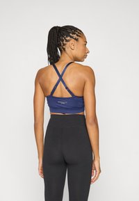 Marineblauwe sportbeha met gekruiste bandjes, aansluitend ontwerp en logodetail. Gecombineerd met zwarte leggings met hoge taille.