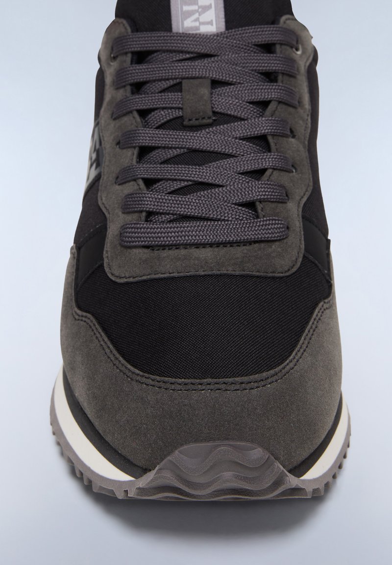 Sneaker grigia realizzata con una combinazione di materiali in suede e nylon, con lacci testurizzati, punta arrotondata e suola in gomma con scanalature diagonali.