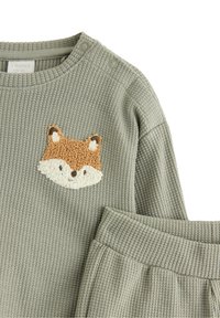 Ein graues, geripptes Stoffset bestehend aus einem Pullover mit einem Fuchs-Gesicht-Patch und passenden Hosen mit elastischem Bund. Die Details umfassen eine strukturierte Naht.
