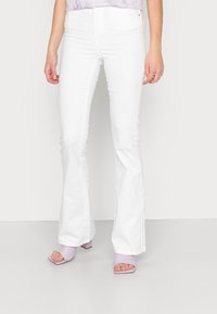 Valkoiset leveälahkeiset farkut korkealla vyötäröllä, joissa on sileä pinta ja siistit linjat. Yhdistetty lila avokas-korkokenkiin, joissa on paksut korot.