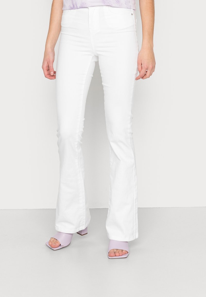 Valkoiset leveälahkeiset farkut korkealla vyötäröllä, joissa on sileä pinta ja siistit linjat. Yhdistetty lila avokas-korkokenkiin, joissa on paksut korot.