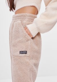 Beige fleece joggingbroeken met een zachte, gestructureerde oppervlakte, zijzakken en een zwart label met "ADV//SEEKER" op de linkerbovenbeen.