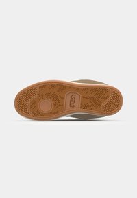Brown rubber sole with a textured pattern, featuring a circular accent and "Fila" logo, bordered by a light tan midsole and upper.