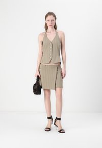 Beige pinstripet halterneck topp med knapper og matchende shorts. Har en skrå lomme, båret med svarte ankelrem-heler og en liten veske.