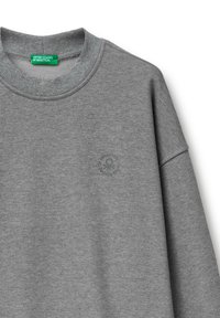 Sudadera gris hecha de tejido suave; presenta un collar y puños acanalados. Pequeño logo circular en gris más oscuro en la parte delantera.
