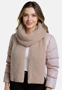 Beige neulehuivi, jossa on ribbikuvio; pehmeä materiaali, paksu muotoilu ja tagi yksityiskohtana alaosassa. Pukeutunut vaaleanpunaisen takin päälle.