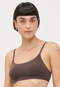 Smeđi bralette napravljen od glatke tkanine. Ima tanke podesive naramenice i jednostavan dizajn bez dodatnih uzoraka ili hardvera.