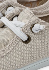 Beige Canvas Slipper mit weißen Schnürsenkeln. Verfügt über runde Metallösen und strukturierte Stoffoberfläche, die ein neutrales, natürliches Aussehen präsentiert.