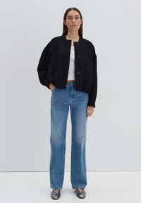 Giacca nera croppata con scollatura rotonda e bottoni, abbinata a jeans dritti blu chiaro e scarpe flat argento. Design minimalista.