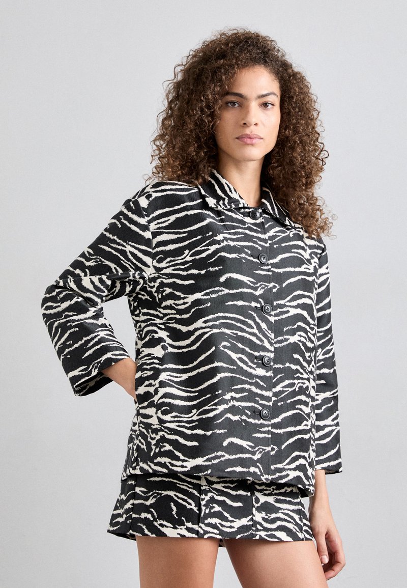 Mustvalge zebra riba muster, kaelusega jakk, mis on nööpidega kinni ja mille juurde kuuluvad sobivad lühikesed püksid. Tekstuuriga kangas, vabalt langev lõige ja 3/4 pikkuses varrukad.